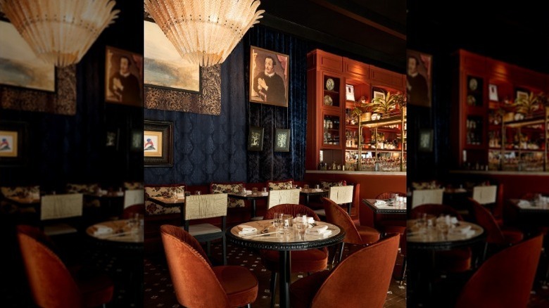 plush red chairs surrounding small circular tables in a room with paintings on the wall