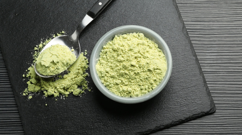 Wasabi powder in small bowl and on spoon on a black background