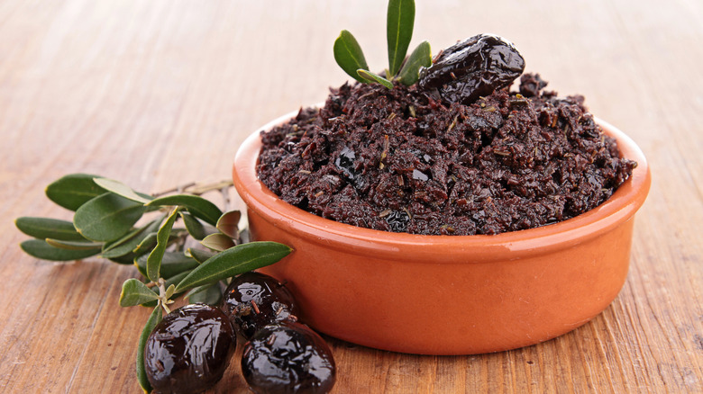 Bowl of black olive tapenade next to whole black olives