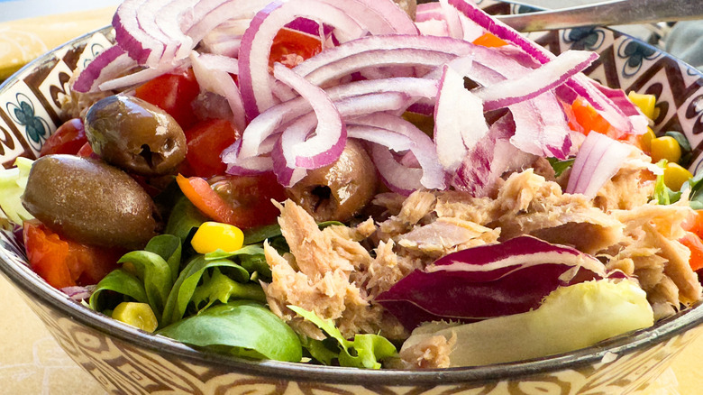 Bowl of tuna salad with sliced red onions, olives, and tomatoes