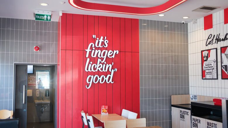 The interior of a KFC restaurant featuring the "It's Finger Lickin' Good" slogan on a red wall