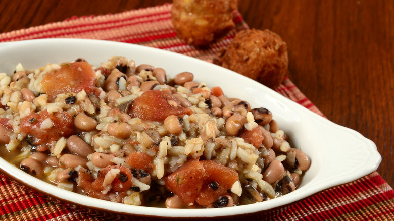 Hoppin' John in white bowl on wooden table with hushpuppies