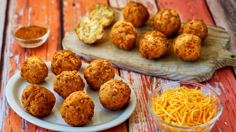 Hushpuppies on a plate and cutting board on picnic table with dish of cheese