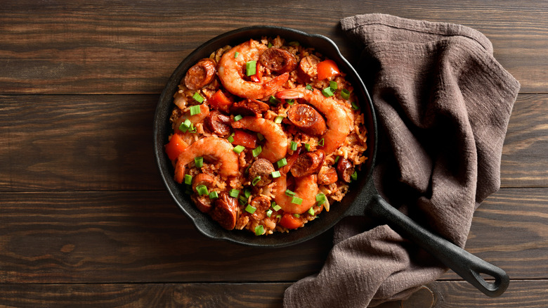 Jambalaya in cast iron pan on wood tabletop background with towel