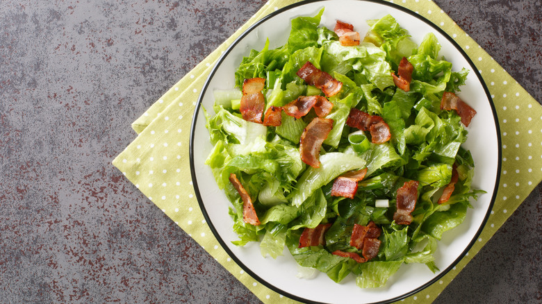 Killed lettuce salad with bacon on plate and stone texture background