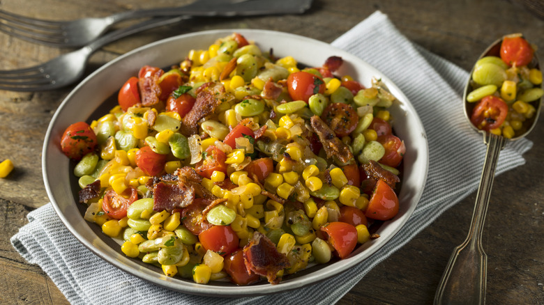 Succotash in bowl on wood table with utensils