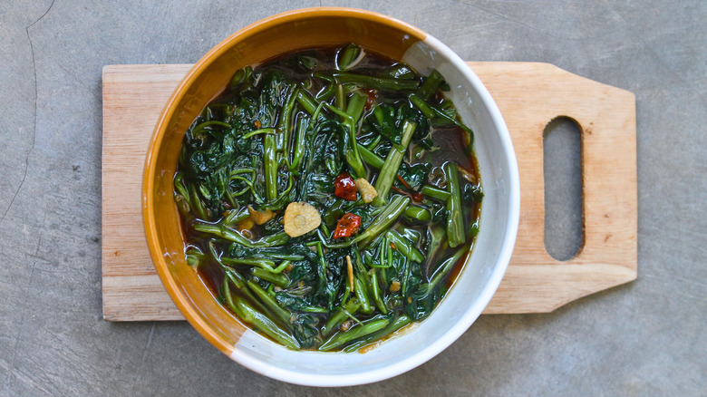 Bowl of stir-fried swamp cabbage on wooden cutting board