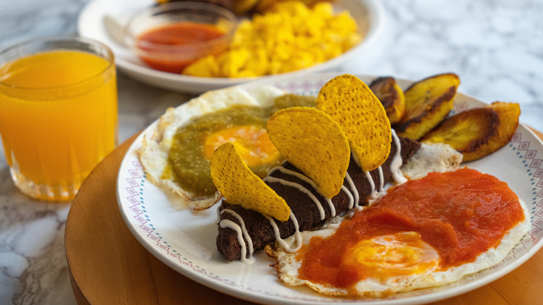 orange juice glass next to spicy breakfast foods on white plates