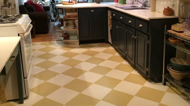 Yellow, painted checkerboard floor in a kitchen with black cabinets and white appliances