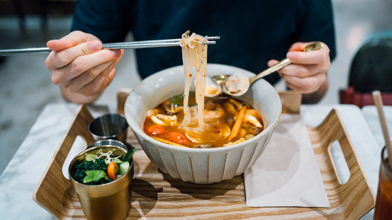 Person eating bowl of spicy Thai soup