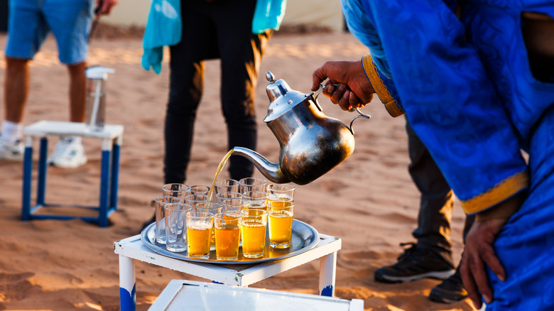 Person pouring glasses of mint tea in the desert