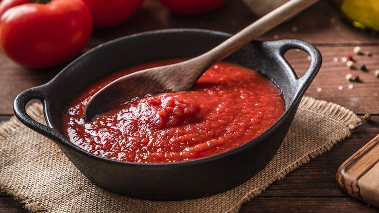 Cast iron black dish full of tomato sauce with wooden spoon and tomatoes in background