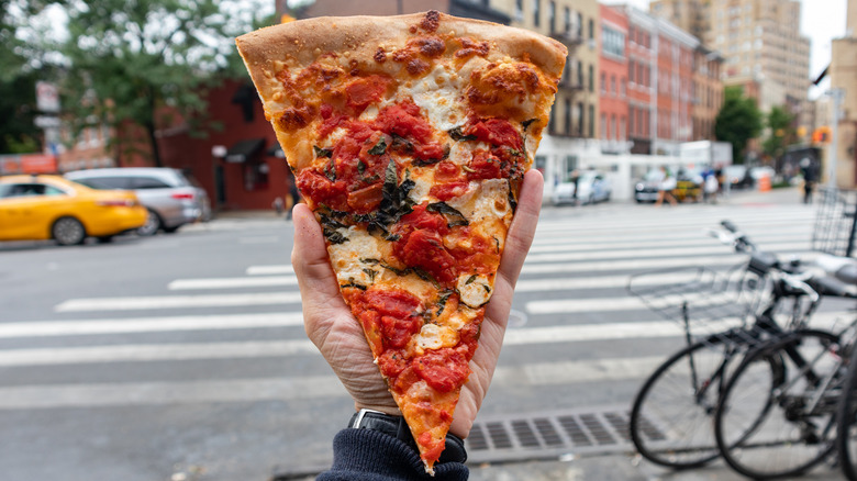 Foodie holding a slice of pizza on a New York City sidewalk