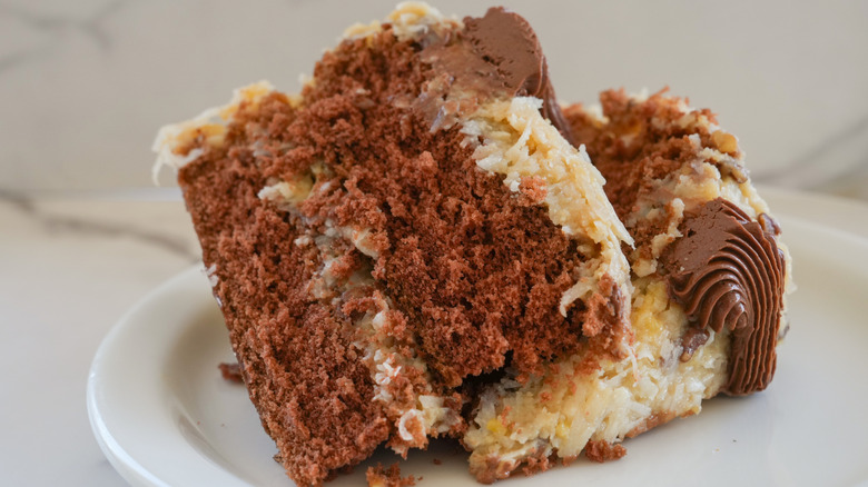 A slice of German chocolate cake on a white plate in front of a marble background