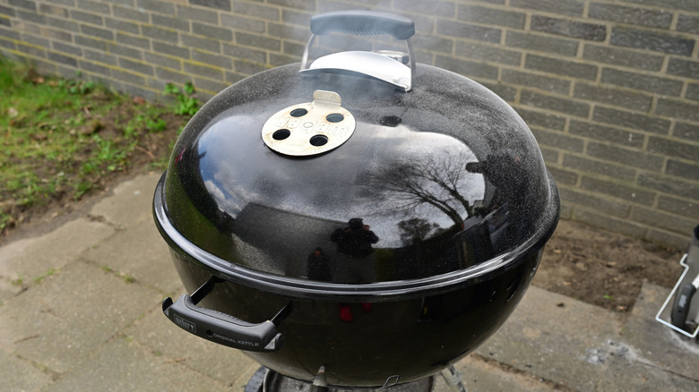 A small black kettle grill with the lid closed and the air vents open