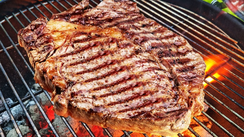 A large steak covered in grill marks cooking over a charcoal grill