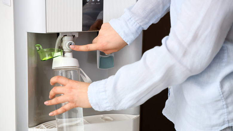 A person fills her water bottle from her home's water cooler