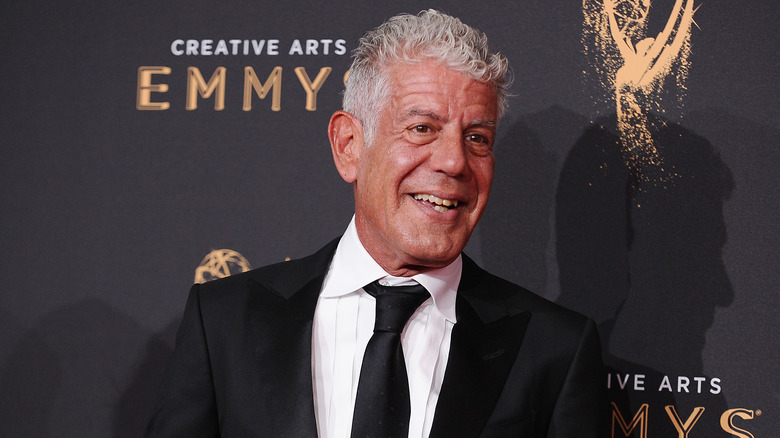 Anthony Bourdain in a black suit and tie smiling in front of a Creative Arts Emmy backdrop