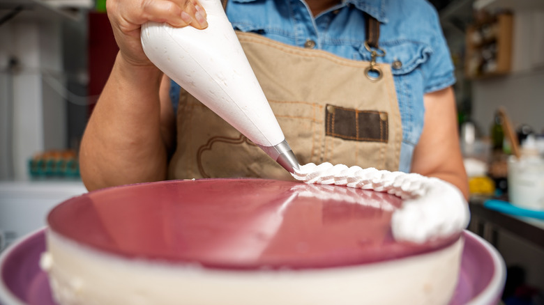 Person piping frosting onto a cake