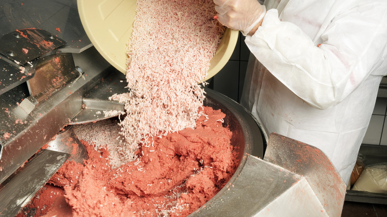 A worker adds fat into a vat of smooth, processed meat