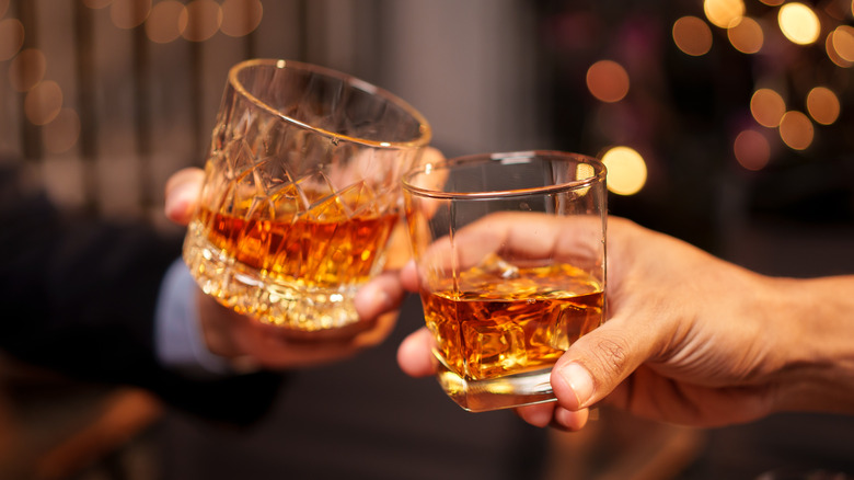 Two hands clinking together glasses of bourbon