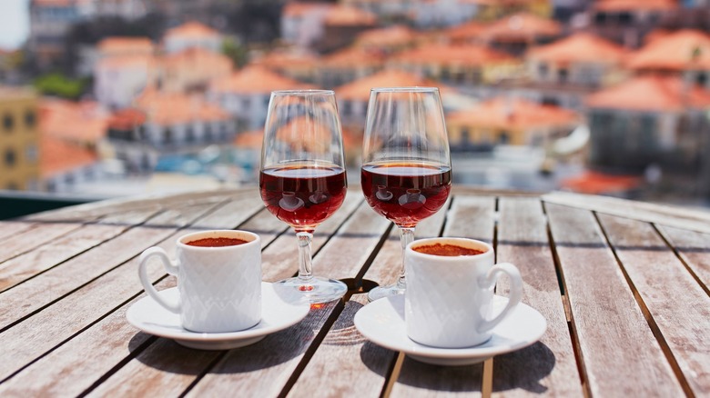 Two glasses of Madeira wine and mugs on a wooden table with Funchal in the background