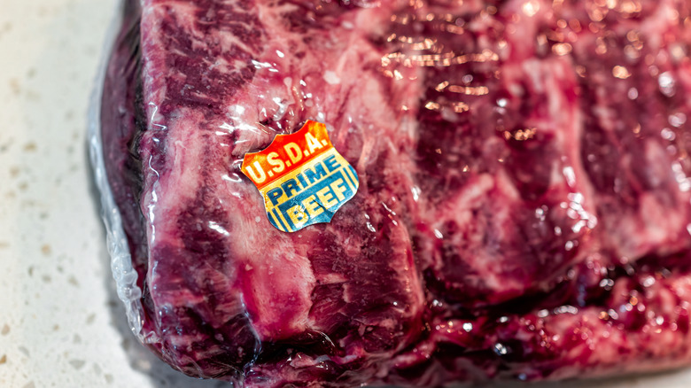 A close-up on a shield-shaped, red, white, and blue sticker that reads "USDA Prime Beef," stuck to a package of meat.