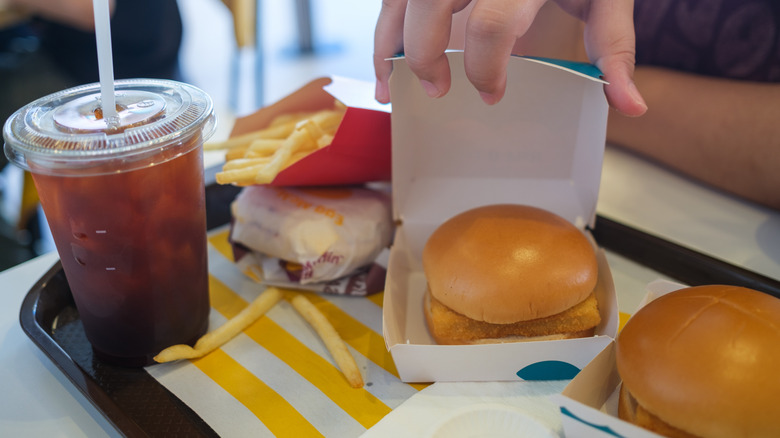 Hand opening a FIlet-O-Fish carton on tray with fries and a drink
