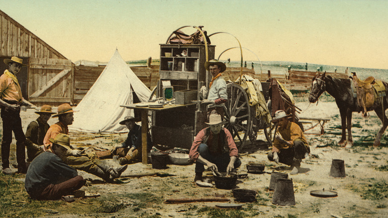 A colorized photograph shows a group of cowboys and horses gathered around a chuck wagon.