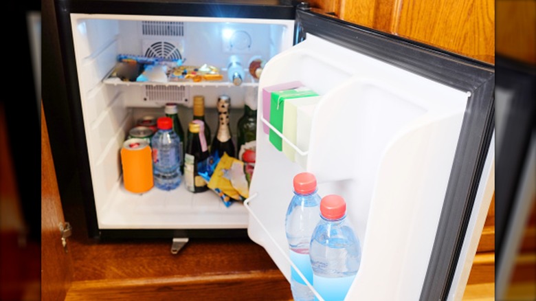 A minibar with the door open revealing drinks and snacks