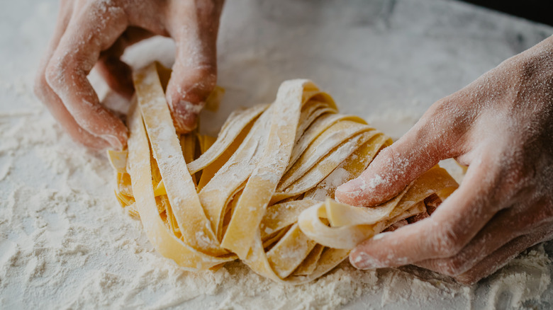 Hands making fresh pasta on a floured countertop
