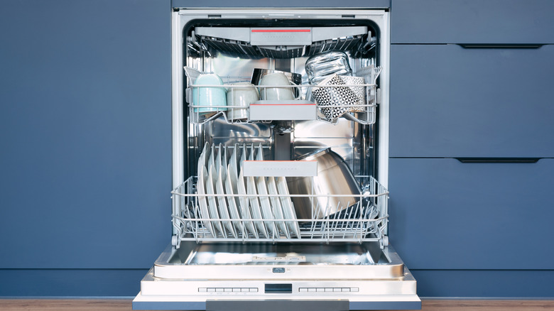 Open dishwasher full of dishes against blue cabinets and drawers in kitchen
