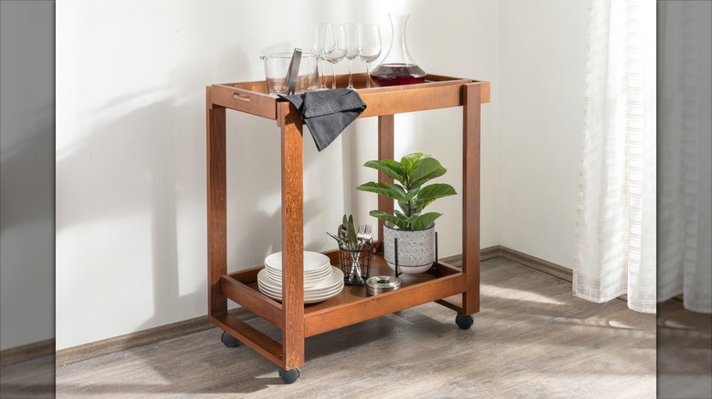 A rolling wooden cart storing wine glasses and wine, plates, and silverware