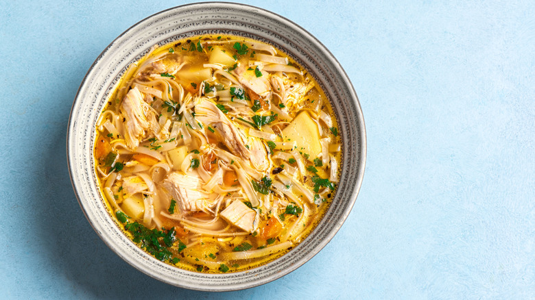 Overhead view of bowl of chicken noodle soup on a blue table surface