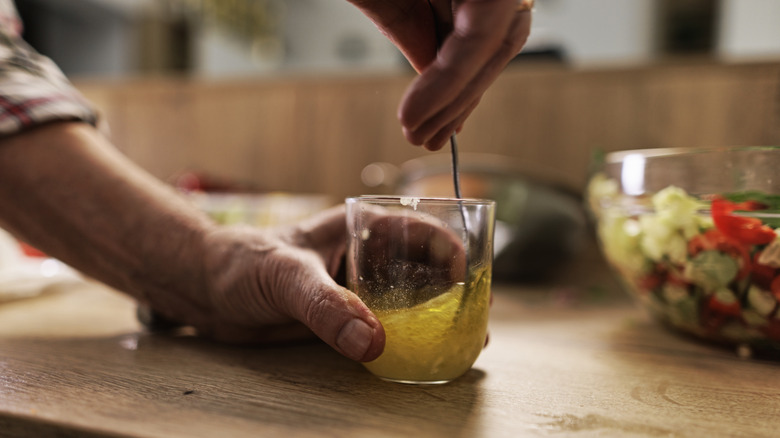 A person uses a for to stir a vinaigrette in a glass