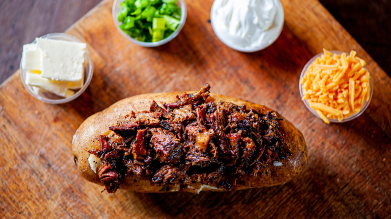 Baked potato stuffed with beef next to bowls of toppings like cheese, sour cream, and green onions