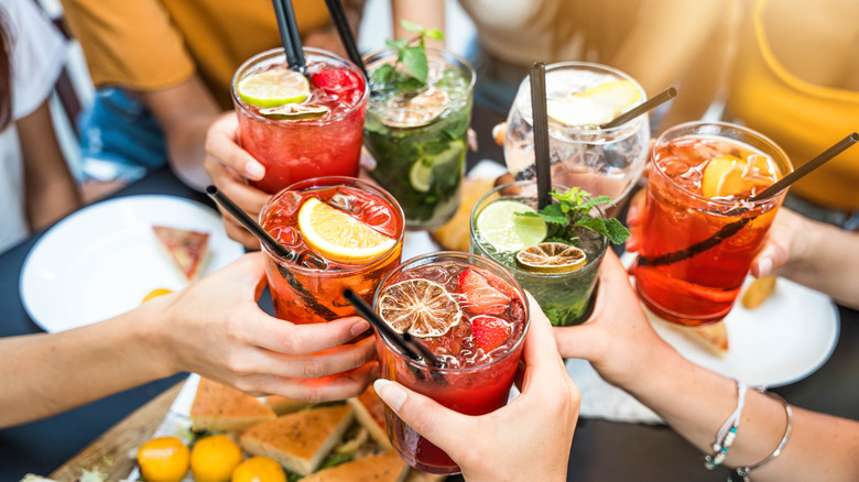 A group of hands toasting with colorful cocktails