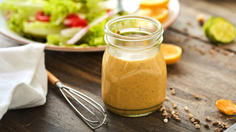 glass jar of salad dressing in front of salad