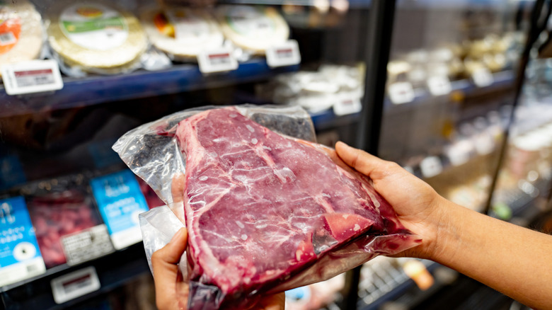 Person holding a packaged steak in a grocery store
