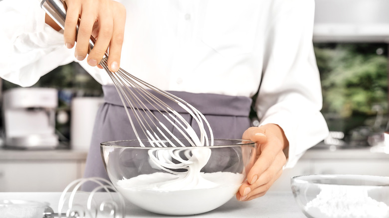 A hand whisking whipped cream in a clear bowl