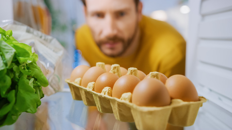 Man peering into fridge with carton eggs