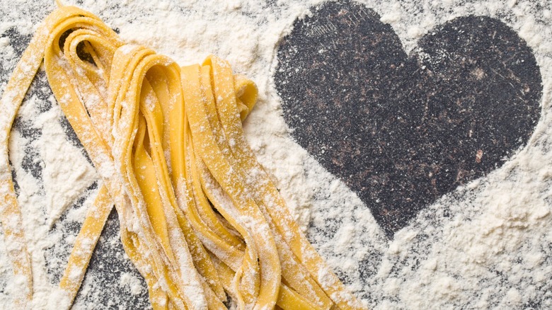 Fresh homemade noodles on a flour covered marble countertop with a heart shape