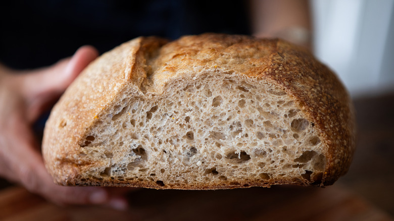A person holding a partially-sliced loaf of bread