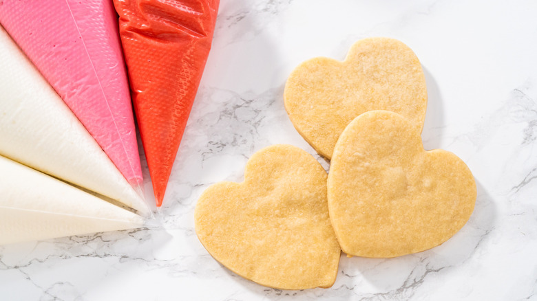 Bags of red and pink royal icing next to heart-shaped sugar cookies