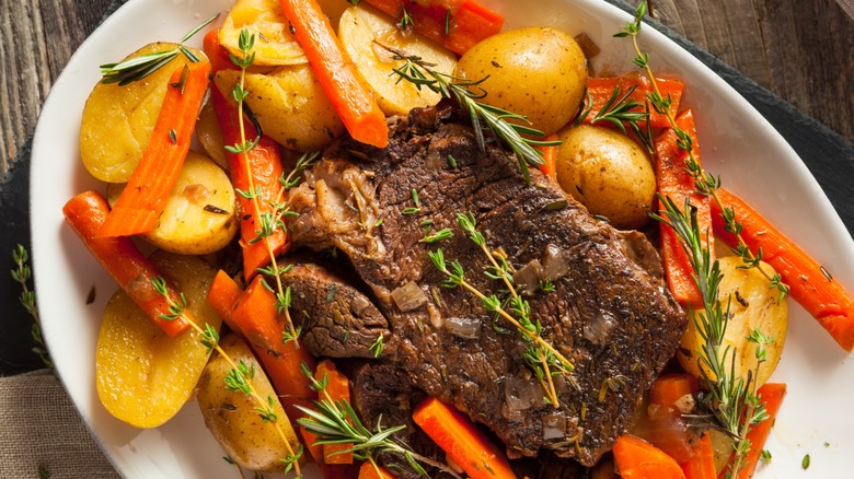 close up of slow cooker pot roast with veggies and herbs on white plate