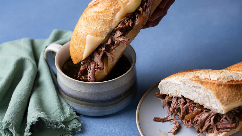 A French dip sandwich is dipped into a bowl of au jus