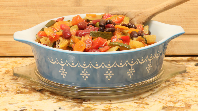 A blue Pyrex casserole dish from the '70s filled with a meal with various vegetables on top