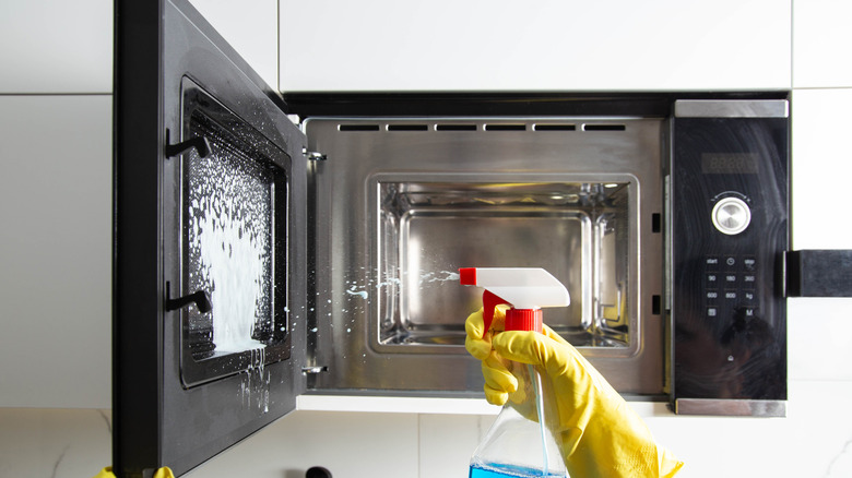 Gloved hand holding a spray bottle spraying into a microwave