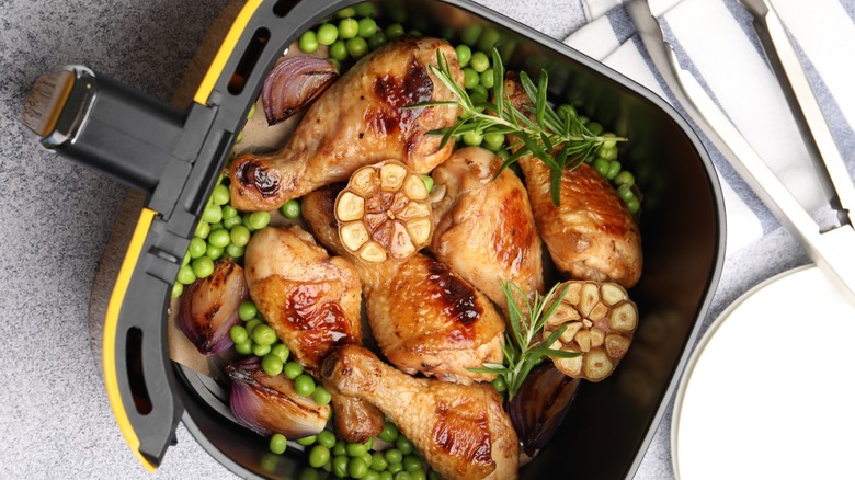 Perfectly crispy chicken drumsticks in an air fryer basket with fresh peas, garlic, and rosemary sprigs