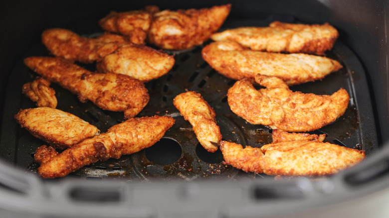A close-up view of small chicken tenderloins, seasoned and cooking in an air fryer basket